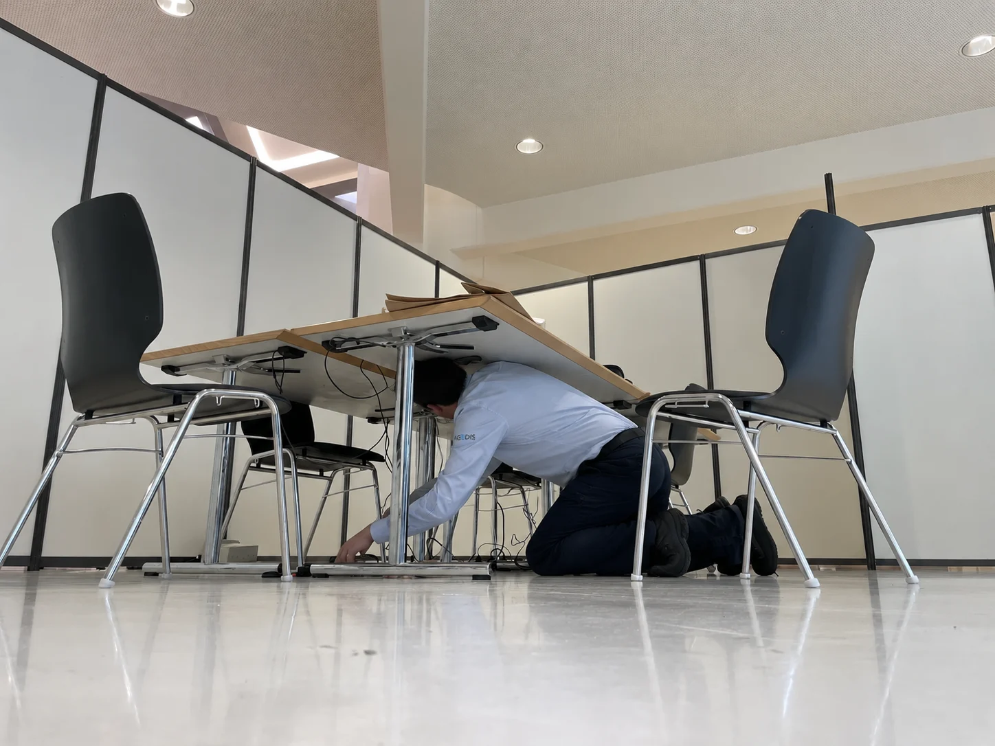Technicien raccordant des postes sous une table, visage masqué par sa position. Photographie d’archives retouchée.